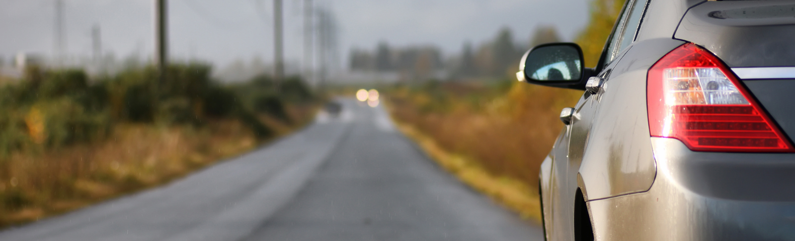 Half of a vehicle on a paved road with headlights in the distance.