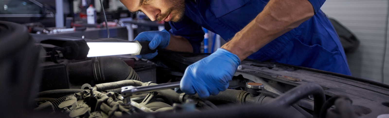 Mechanic working on an engine holding a light and tool.