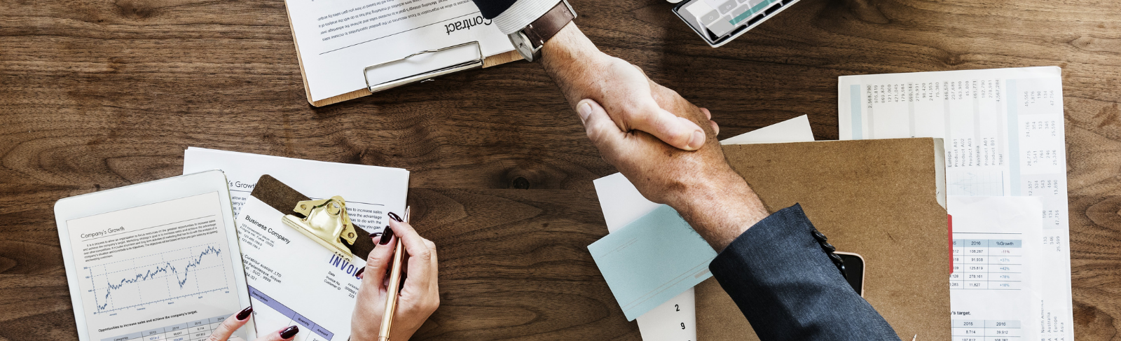 Aerial shot of two people shaking hands above a work station with papers, pens etc.