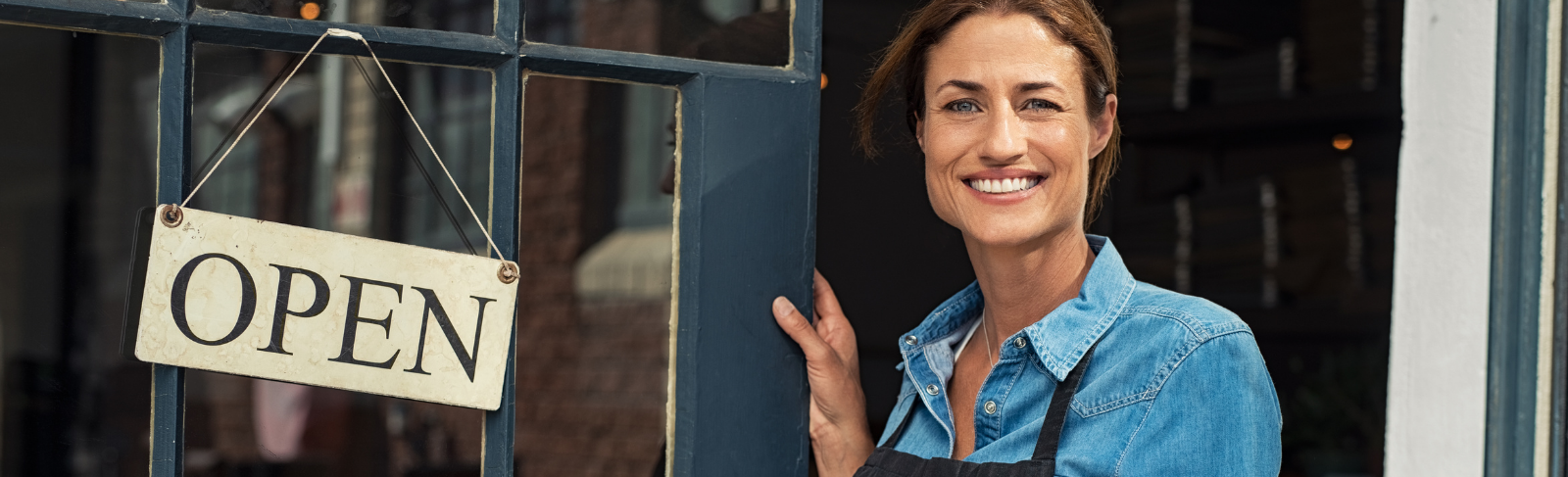 Business owner holding a door open with an open sign hanging on the door.