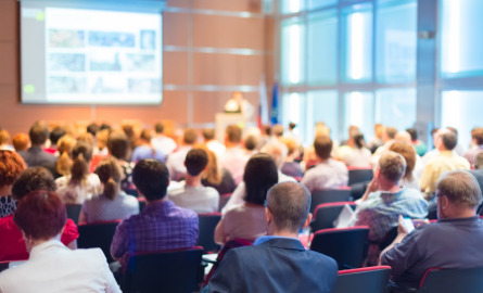 A presentation room filled with people watching a presentation on a screen.