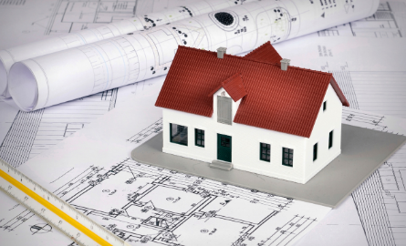 A miniature house on a pile of draft papers. 