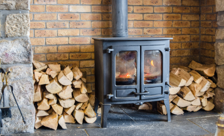 An indoor wood stove with piles of wood on either side.