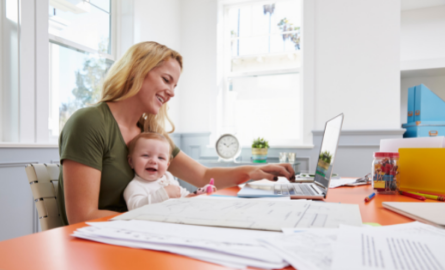 Working mom holding a baby while working on a computer.