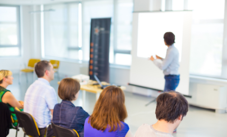 A presenter in front of a screen teaching a group of people.