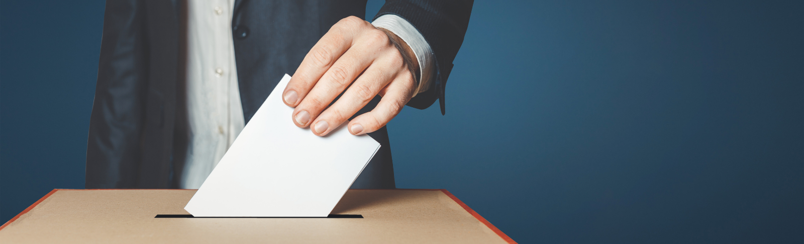 A hand placing a voter ballot into a box.