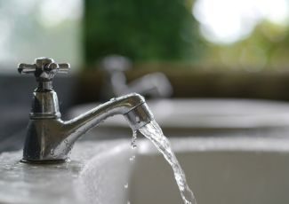 An open sink faucet with water pouring out.