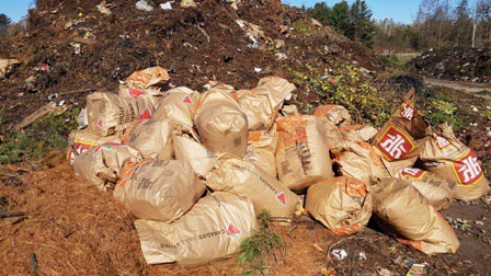 A mound of dirt with a pile of compostable leaf bags ready for composting.