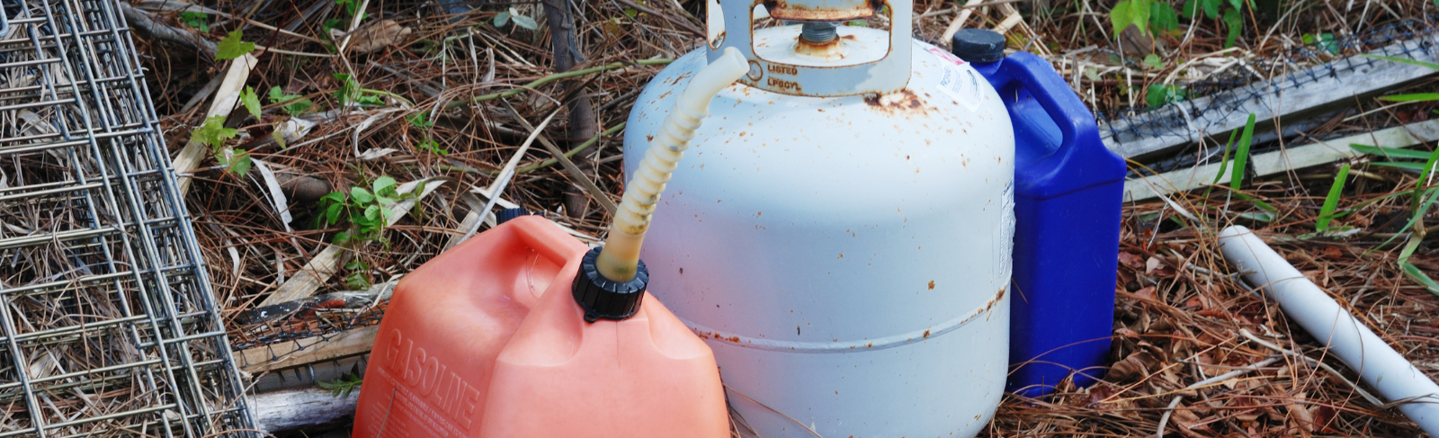 A propane canister and gasoline caddy on the ground outdoors.