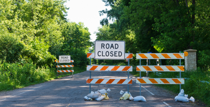 Road closed sign with barricades blocking a road.