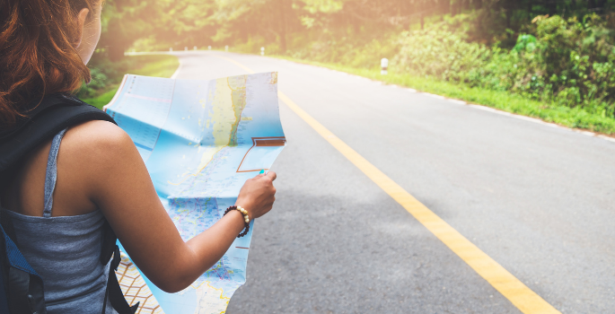 Girl standing on a road looking at an open road map.