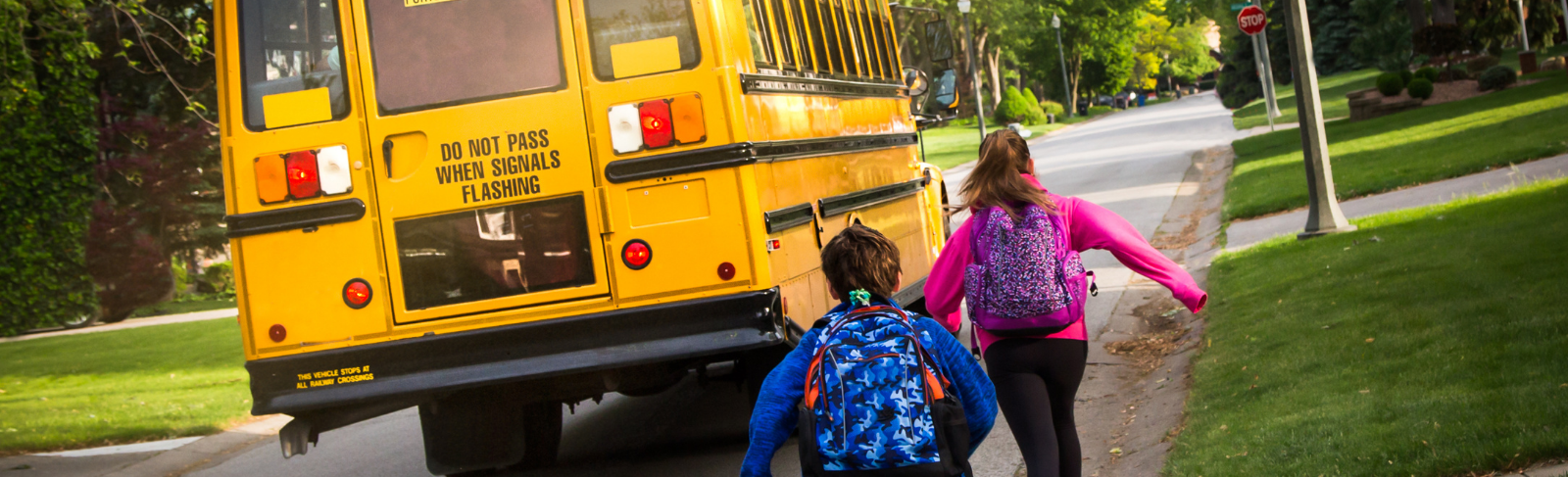Two kids running for a yellow school bus.