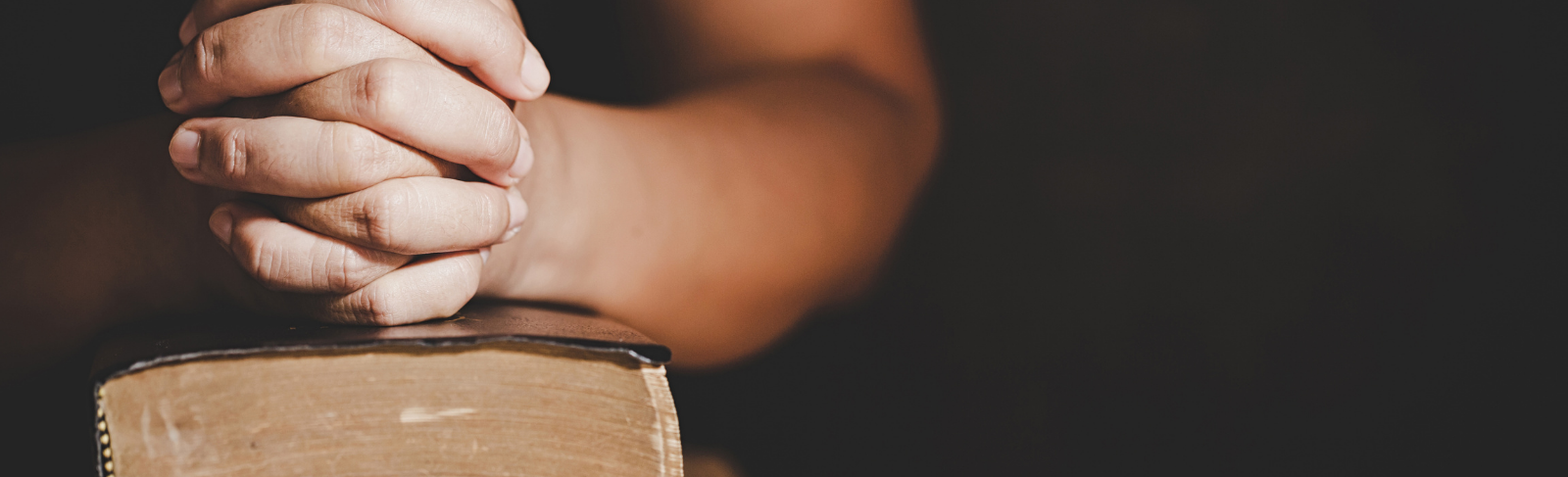 Hands clasped together resting atop a book of worship.