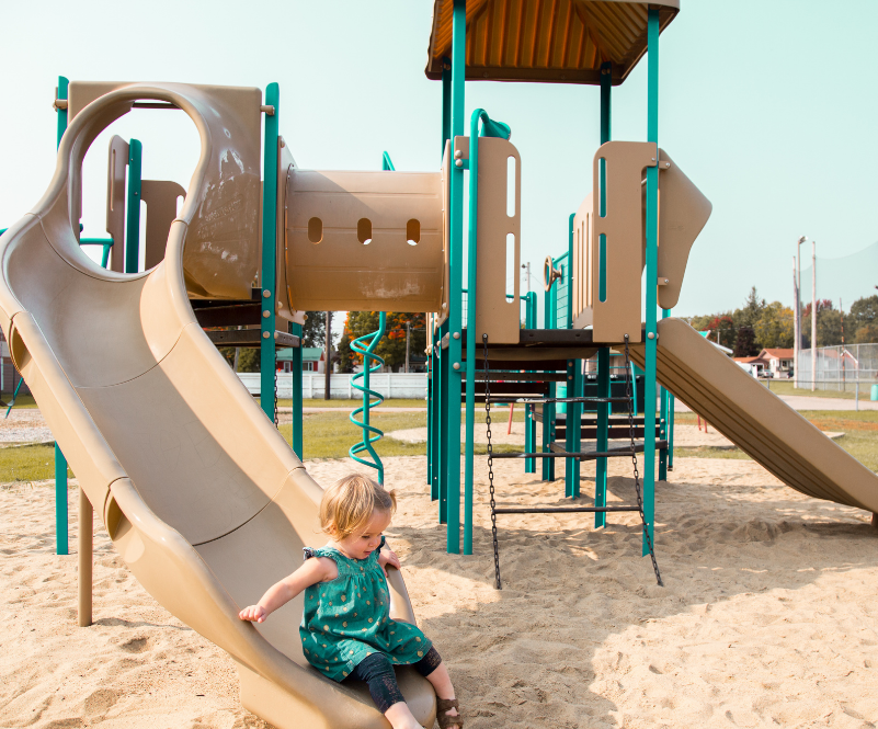 Little girl going down a slide on a play structure.